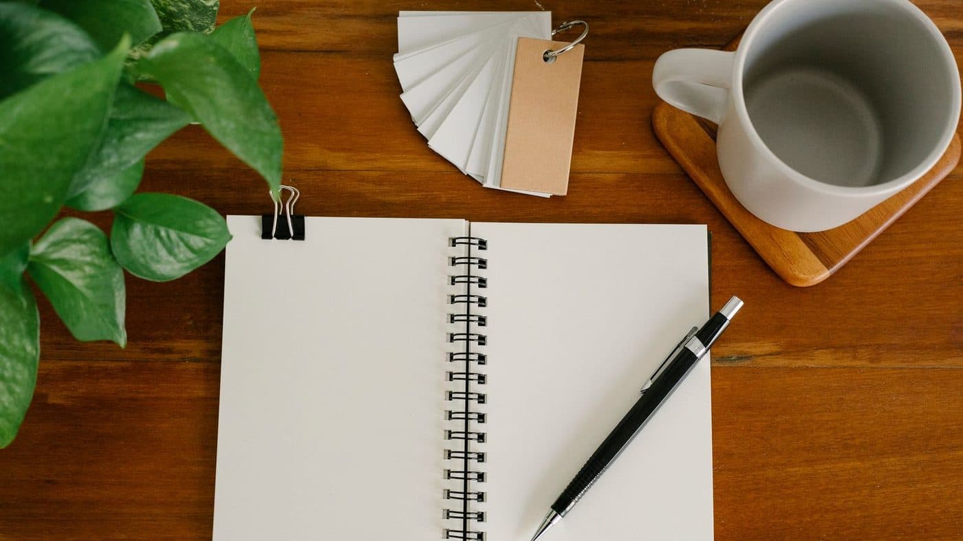 An open notebook, pen and mug on a wooden desk
