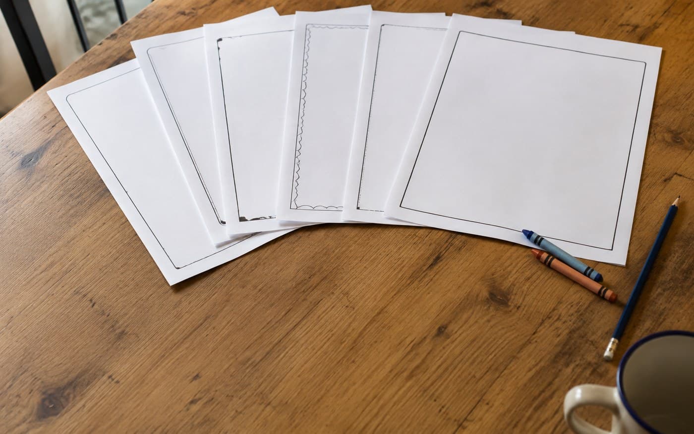 Printed worksheets fanned across a kitchen table with crayons at the edge