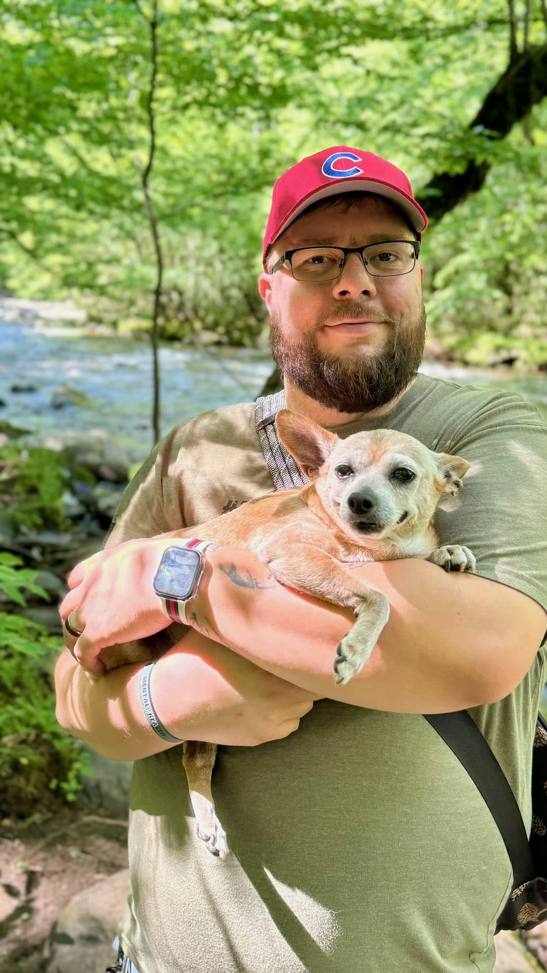 Brian Palermo holding Bobo in his arms on a wooded trail beside a stream