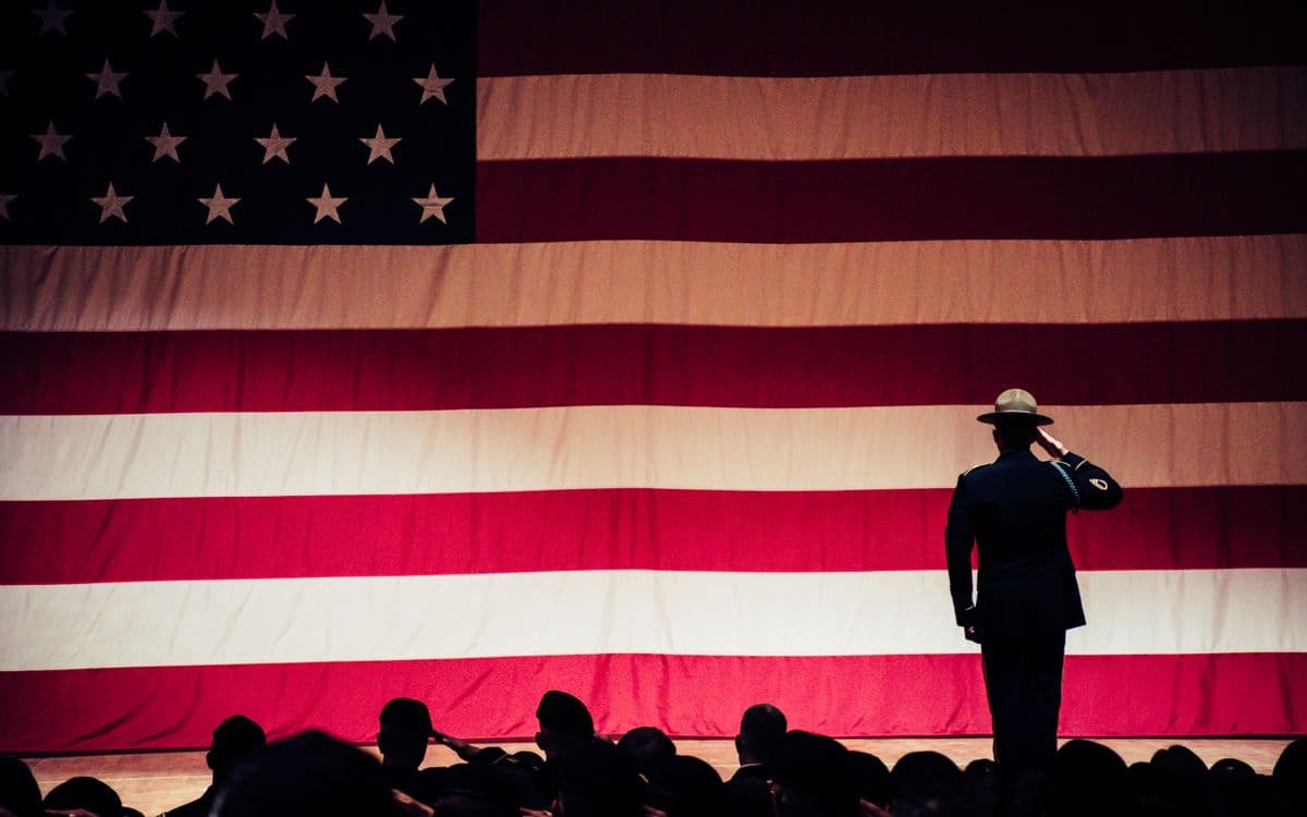 A service member saluting in front of a large American flag at a ceremony