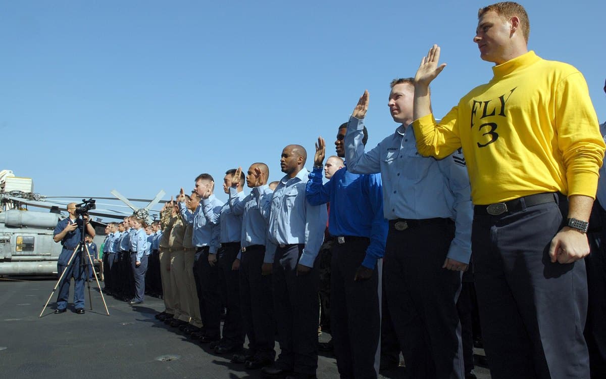 A line of sailors with right hands raised, taking the oath on a carrier deck