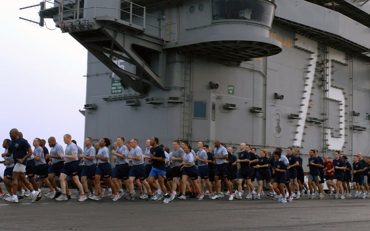 Sailors running together on a carrier flight deck in the early morning